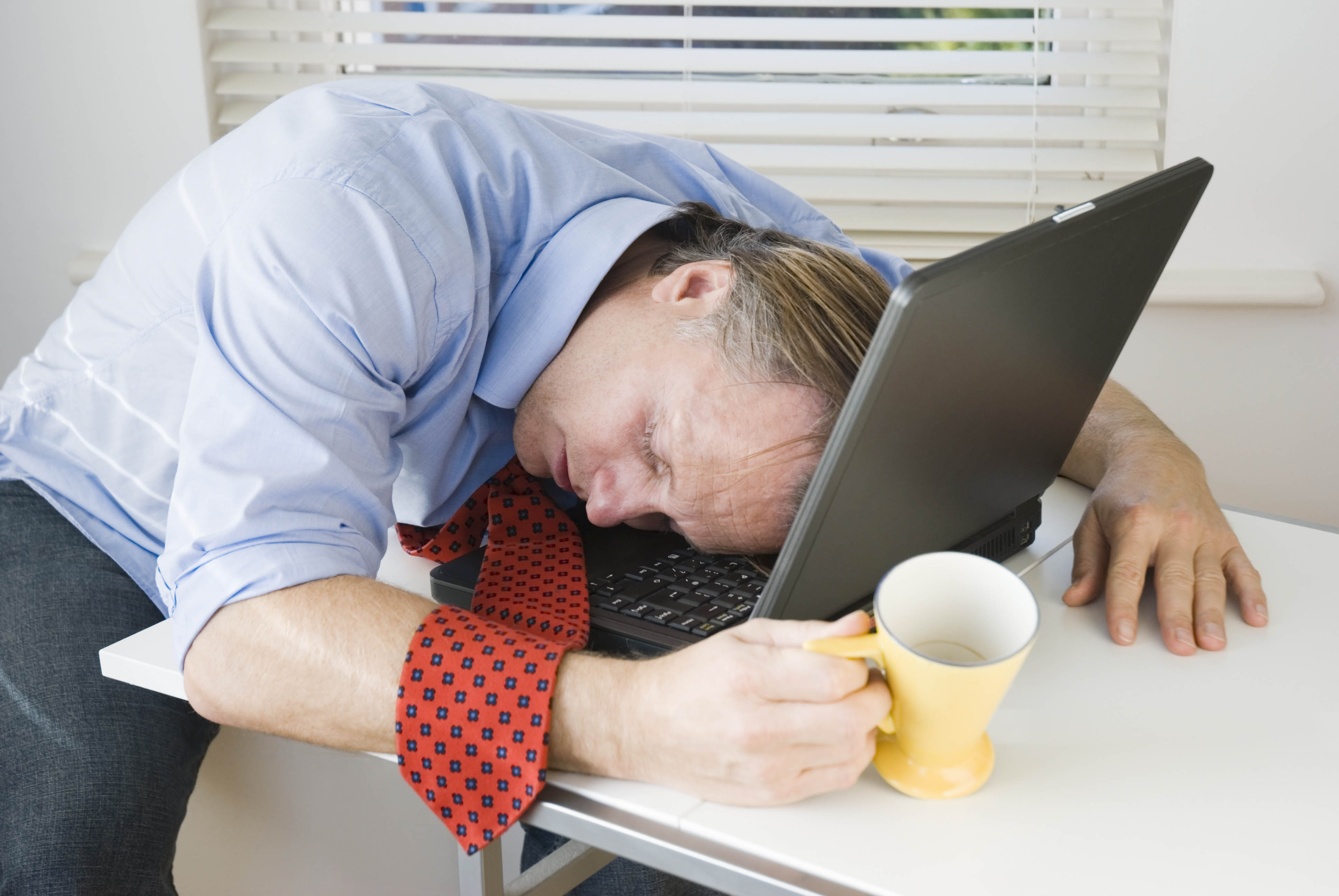 Man in his work clothes, sleeping on his laptop at the table